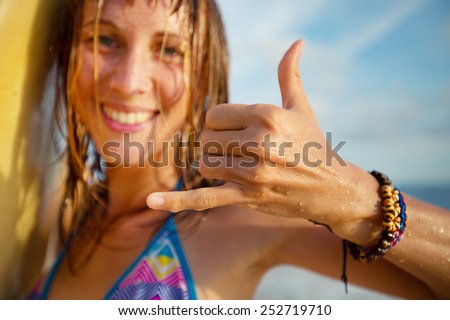 Happy smiling lady surfer showing shaka sigh. Focus on the hand