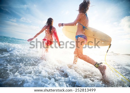 Two young ladies surfers running into the sea with surf boards