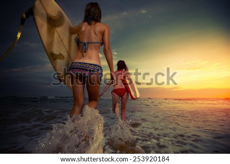 Two young ladies surfers running into sea with surf boards