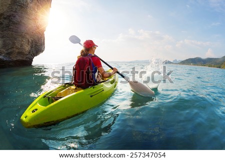 Young lady paddling the kayak near the cliff at sunny day