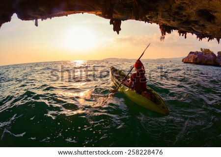 Young lady paddling the kayak from limestone cave towards open sea