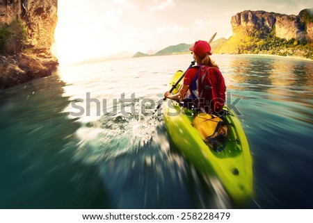 Young lady paddling the kayak in a bay with limestone mountains. Motion blurred water surface