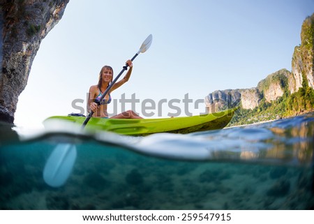 Young lady paddling the kayak in a bay with limestone mountains. Split shot with underwater view