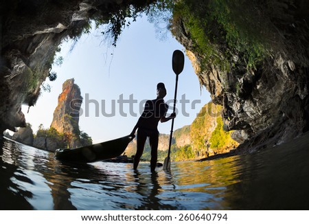 Silhouette of the young lady entering marine cave with kayak