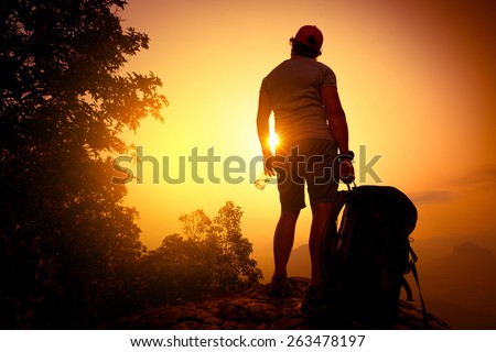 Backpacker standing on top of the mountain with bottle of water at sunrise