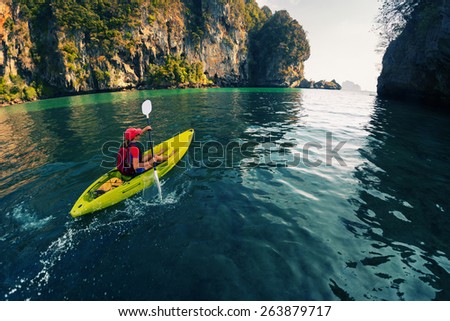 Young lady paddling the kayak in the calm bay with limestone mountains