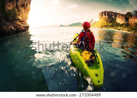 Young lady paddling the kayak in a calm bay with limestone mountains