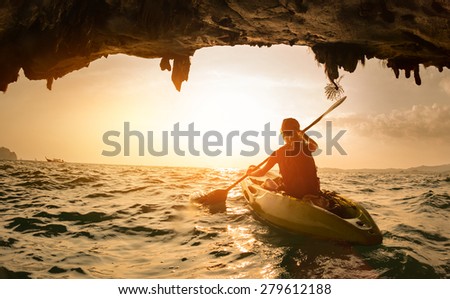 Young lady paddling the kayak in a sea near the cave exit