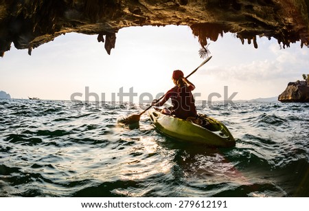 Young lady paddling the kayak in a sea near the cave exit