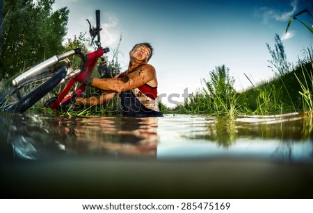 Young man athlete with dirty stained clothes crossing the swamp with bicycle