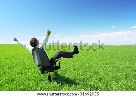 Happy businessman on chair in green field