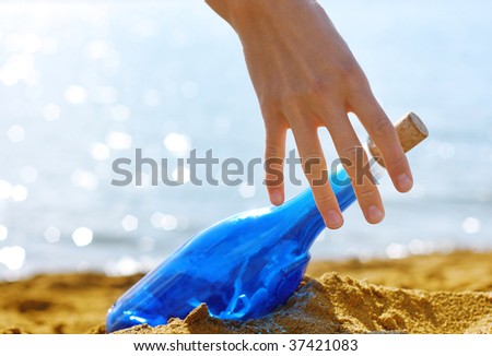 Blue glass bottle in yellow sand with hand