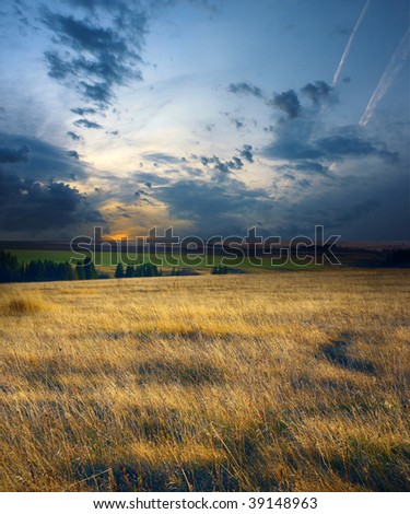 Sunset on dry field with dark blue storm clouds