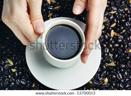 Cup with coffee in hands over coffee beans background