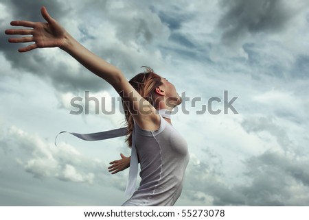 stock photo : Young woman in white shirt with raised hands over stormy cloudscape