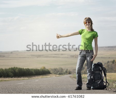 Young smiling woman with backpack catching a car on empty road