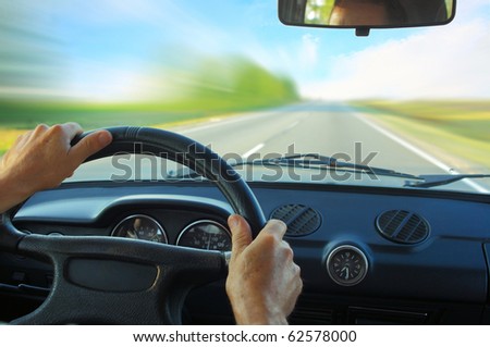 Driver in car holding steering wheel. Blurred road and sky