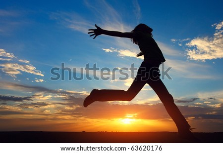 Young jumping woman with raised hands on sunset