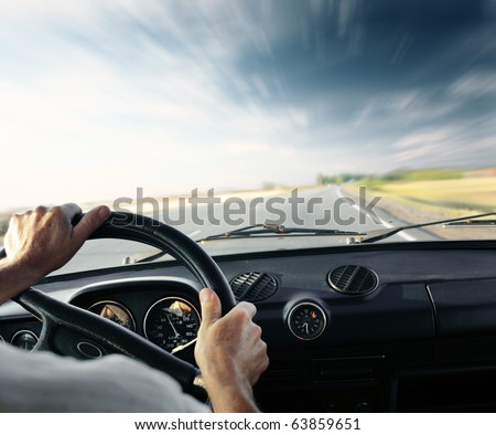 Driver\'s hands on a steering wheel of a car and blue sky with blurred clouds