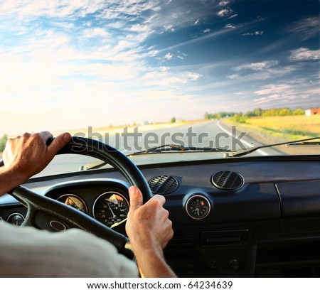 Driver\'s hands on a steering wheel of a car and blue sky with clouds