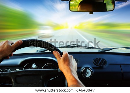 Hands on steering wheel of a car driving on an asphalt blurred road