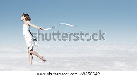 Young woman in white dress with white ribbon walking in a clouds