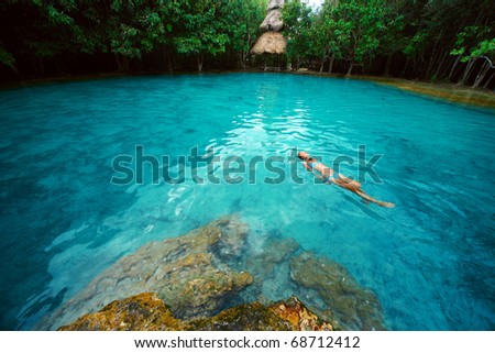 Young woman swimming alone in a blue clear water of a lake situated in tropical forest