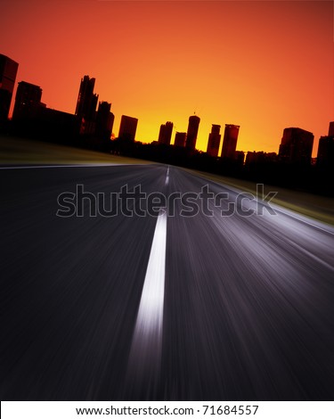 Asphalt blurry road with city silhouette on a horizon and red sunrise sky