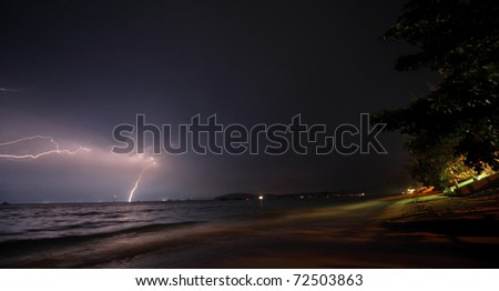 Flash in dark night sky over sea and yellow coast