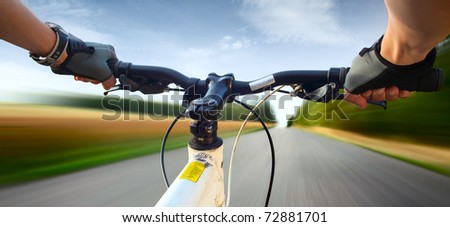 Hands in gloves holding handlebar of a bicycle. Motion blurred asphalt road