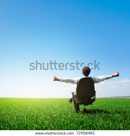 Man sitting on chair on green meadow on blue clear sky background
