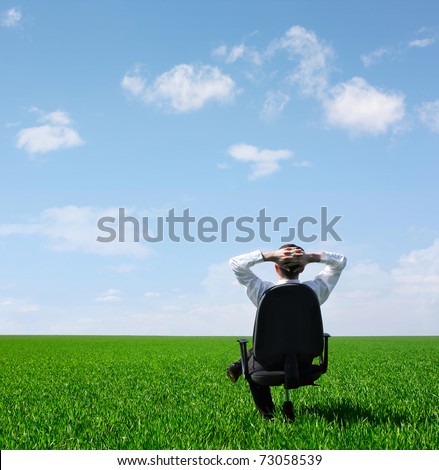 Man sitting on chair on green meadow on blue cloudy sky background