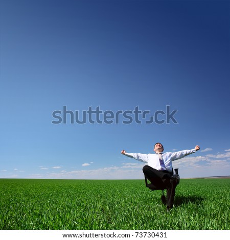 Man sitting on chair on green meadow on blue clear sky background