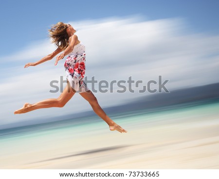 Young woman in summer dress jumping on sand. Motion blurred background