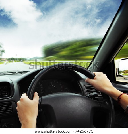Hands on steering wheel of a car and motion blurred asphalt road and sky