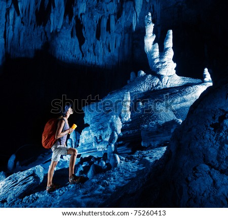 Young woman with backpack exploring huge cave with torch