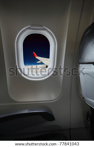 Interior of a plane with sky view and red wing in window