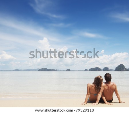 Young family sitting on white sand by sea and looking to the horizon