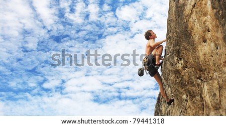 Young man climbs on a cliff over blue sky background