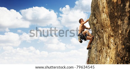Young man climbs on a cliff over blue sky background