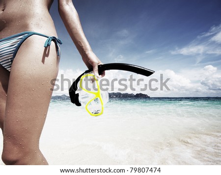 Young woman with wet skin holding a mask and snorkel standing by blue sea