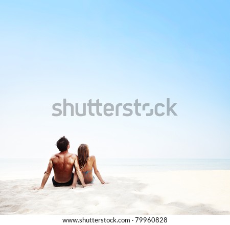 Young family sitting on white sand by sea and enjoying each other