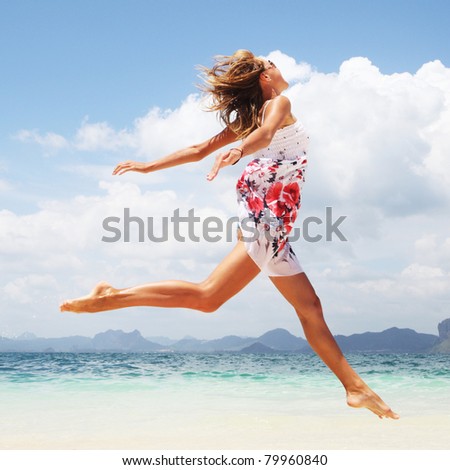 Woman in summer dress jumping over wet sand by tropical sea