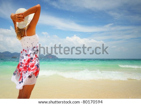 Woman in summer dress standing on wet sand by tropical sea