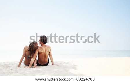 Young family sitting on white sand by sea and enjoying each other