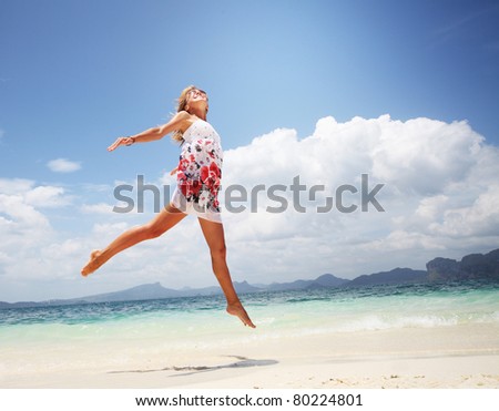Woman in summer dress jumping over wet sand by tropical sea