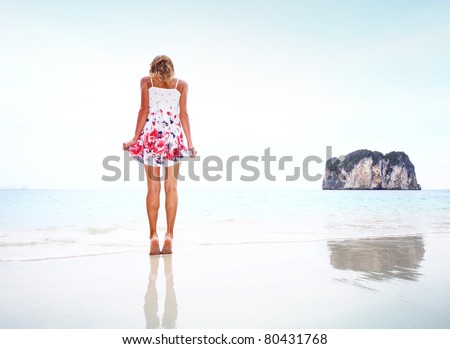 Young woman in summer dress standing on wet perfect sand and looking to her feet
