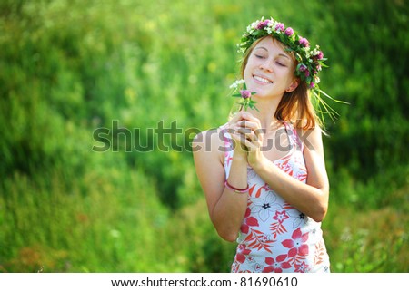 Young smiling woman with wreath holding a clover flower on green background