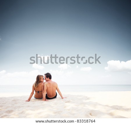 Young happy couple sitting on a sand by sea and enjoying each other