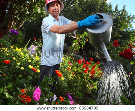 Mature caucasian smiling man watering her garden with a lot of flowers